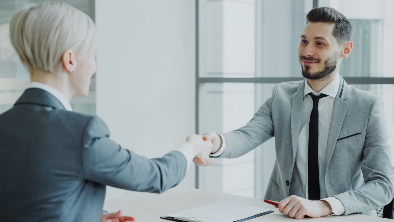 Two professionals shaking hands in a bright, modern office environment.